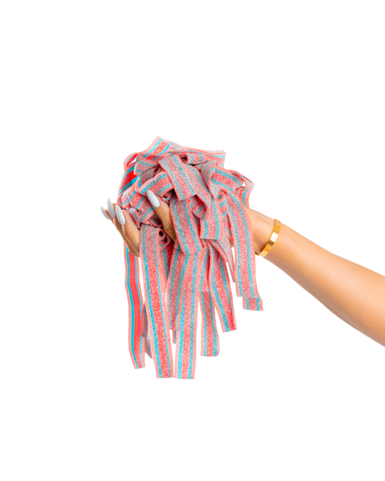 A hand with long, manicured nails and a gold bracelet holds a bunch of colorful SourStrips Dreamberry-Six Pack sour strips against a plain white background.
