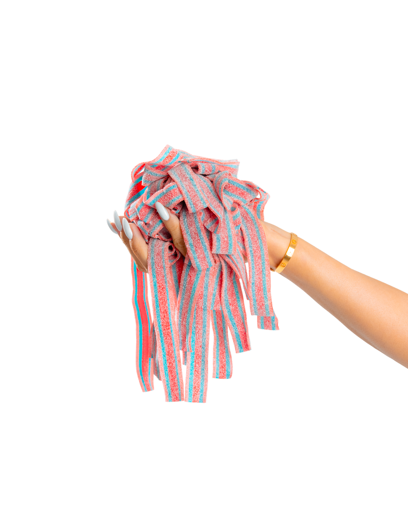 A hand with long, manicured nails and a gold bracelet holds a bunch of colorful SourStrips Dreamberry-Six Pack sour strips against a plain white background.