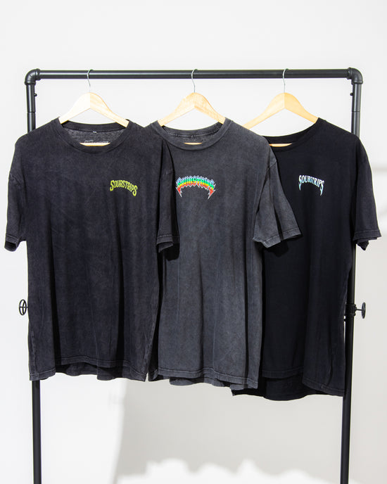 Three black SourStrips Sour Storm Tees with unique graphics hang on wooden hangers from a black rack, showcasing the perfect unisex cotton style against a crisp white background.