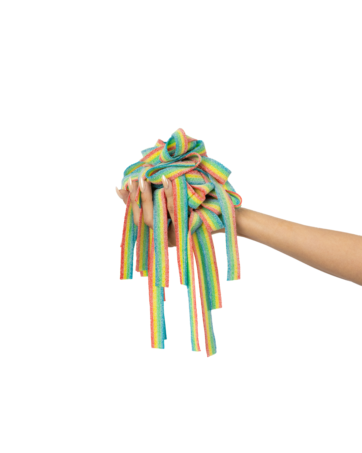 A hand holds a bundle of rainbow-colored, sugar-coated candy strips against a vibrant background that transitions from green to yellow to orange. The candy strips are long and appear to be flexible, showcasing bright, multicolored stripes.