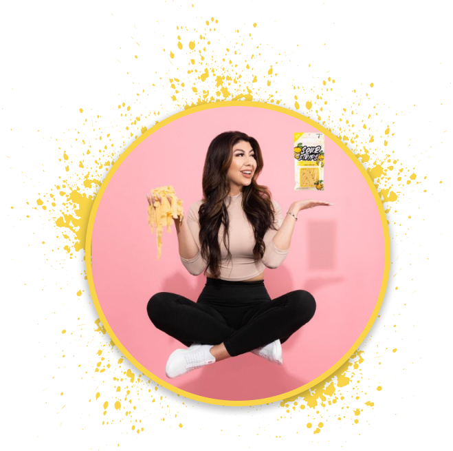A woman with long hair levitates cross-legged against a pink background. She holds a handful of chips in one hand and a bag of "Chipoys" in the other, smiling brightly. A yellow splattered ring encircles her.