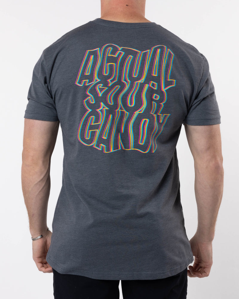 A person wearing the Trippy Tee by SourStrips, a dark gray, relaxed-fit T-shirt with "ACTUAL SOUR CANDY" written on the back in bold, distorted, colorful letters. The super soft cotton graphic T-shirt drapes comfortably as they face away from the camera, showcasing the vibrant design.