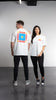 Two individuals pose in casual attire against a grey backdrop. The person on the left is facing away, revealing vibrant graphics and text saying "SOUR" on the back of their oversized box fit Sunshine Tee from SourStrips. The person on the right faces forward, wearing a white Sunshine Tee with subtle text on the front, showcasing a unisex design by SourStrips.