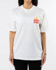 A person wearing a white Sunshine Tee with a small red and yellow "SourStrips" logo on the upper left side stands against a plain white background. The unisex design pairs seamlessly with their black pants, their hands resting by their sides.