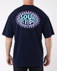A person stands facing away, wearing an oversized box fit black Solar Tee from SourStrips. The unisex design features a colorful graphic on the back with the text "SOUR STRIPS" in blue and pink within a circular design bordered by a pattern of pink crescents. The background is plain white.