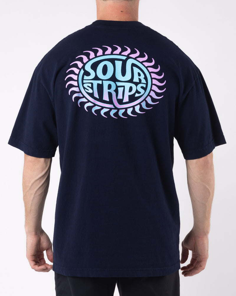 A person stands facing away, wearing an oversized box fit black Solar Tee from SourStrips. The unisex design features a colorful graphic on the back with the text "SOUR STRIPS" in blue and pink within a circular design bordered by a pattern of pink crescents. The background is plain white.